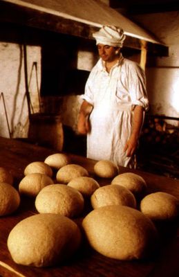 Photo of a baker standing with bread loaves and oven, Fortress of Louisbourg National Historic Site